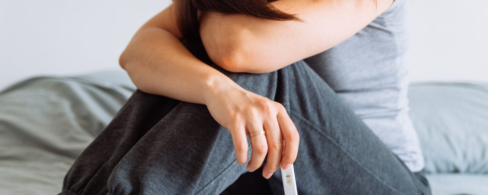 sad woman on bed with negative pregnancy test